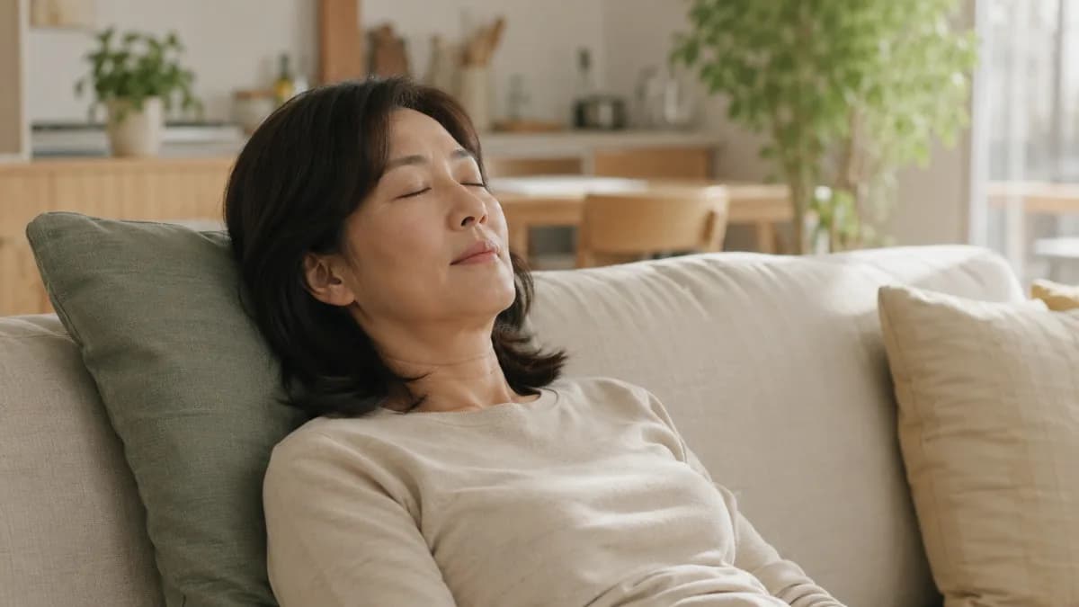 오후 거실 소파에 앉아 햇빛 속에서 눈을 감고 잠시 쉬는 50대 한국 여성
