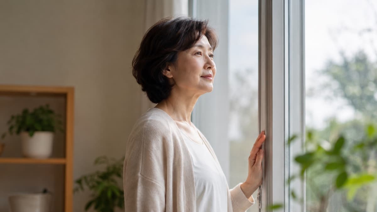 창가에 서서 창밖을 바라보며 숨을 고르는 여성