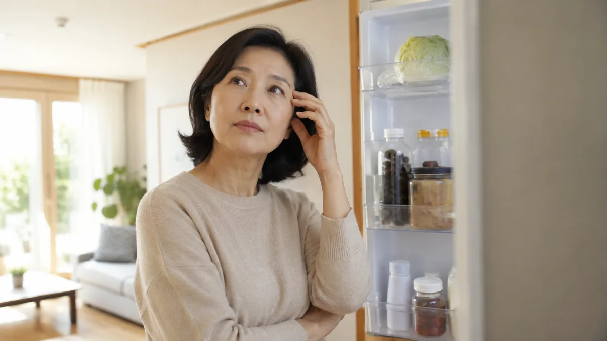 부엌에서 냉장고 문을 열어 둔 채 잠시 생각에 잠긴 50대 한국 여성